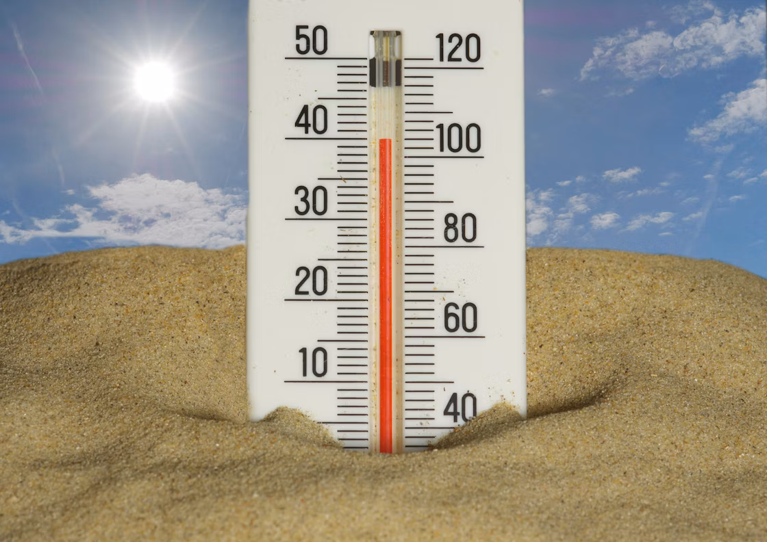 an image of a thermometer in the foreground partially buried in sand, and blue sky in the background. The temperature on the thermometer is nearing 40C