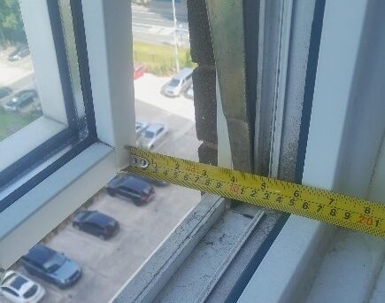 An open window with a tape measure showing the maximum opening with a safety restrictor engaged.