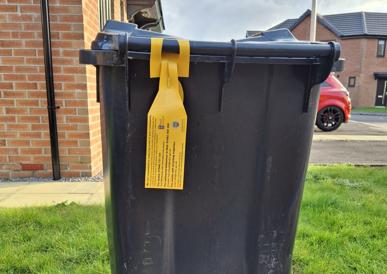 A black household waste bin with a yellow tag.