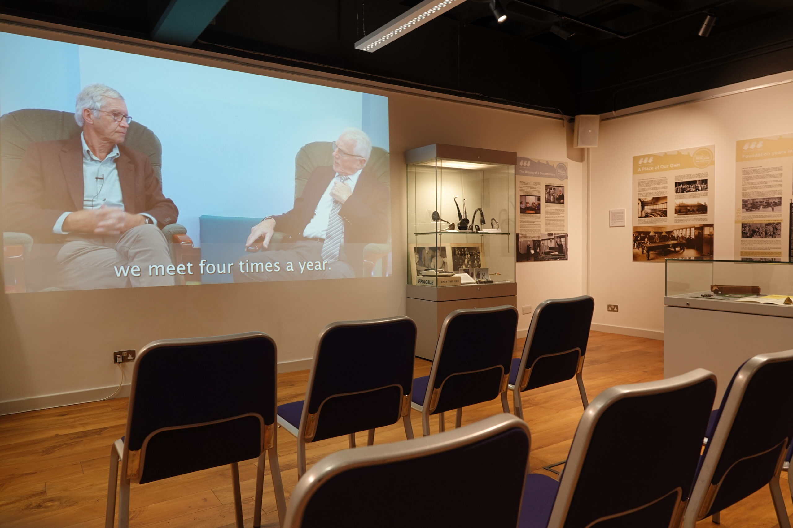 The image shows the documentary playing in the background, with some of the infoation boards on show.