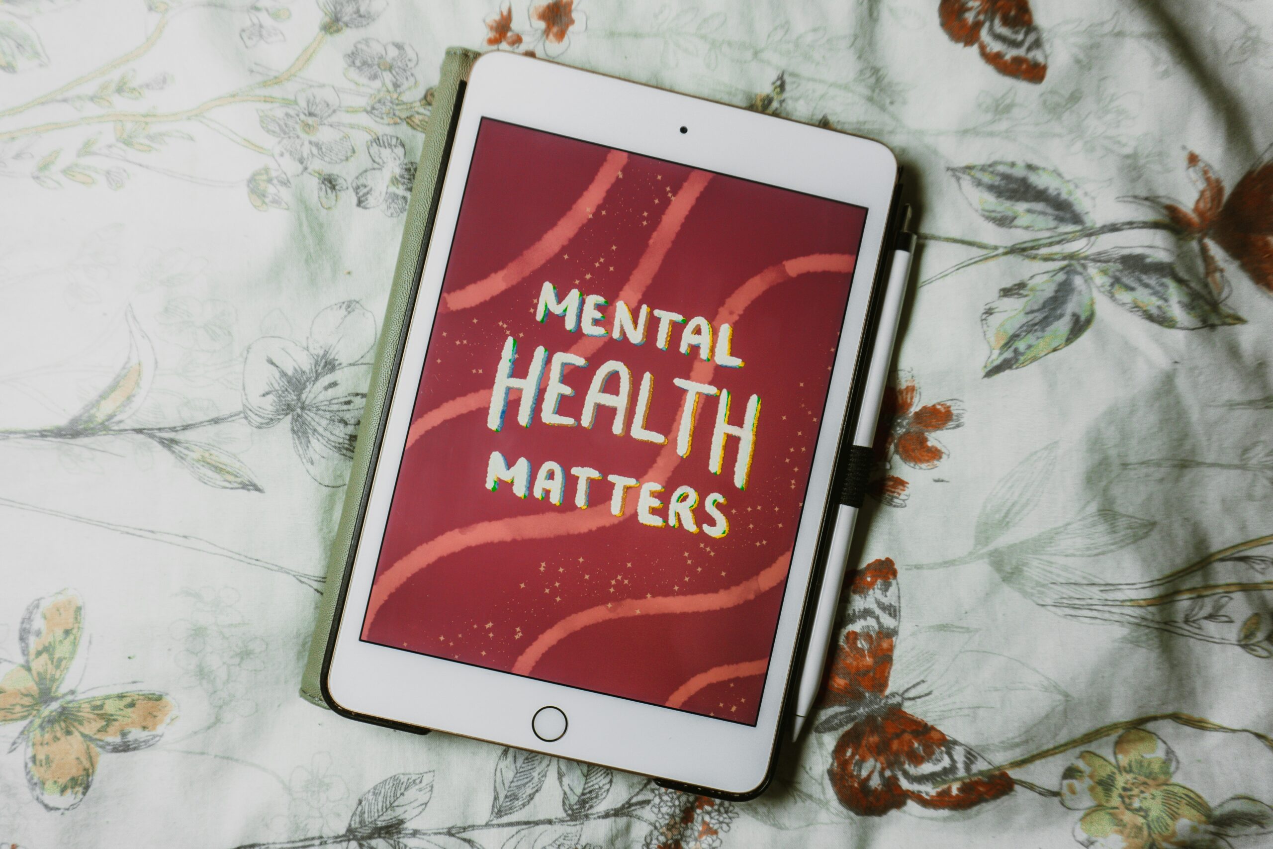 A tablet resting on patterned bedding. On the tablet, white text on a red background reads 'mental health matters'