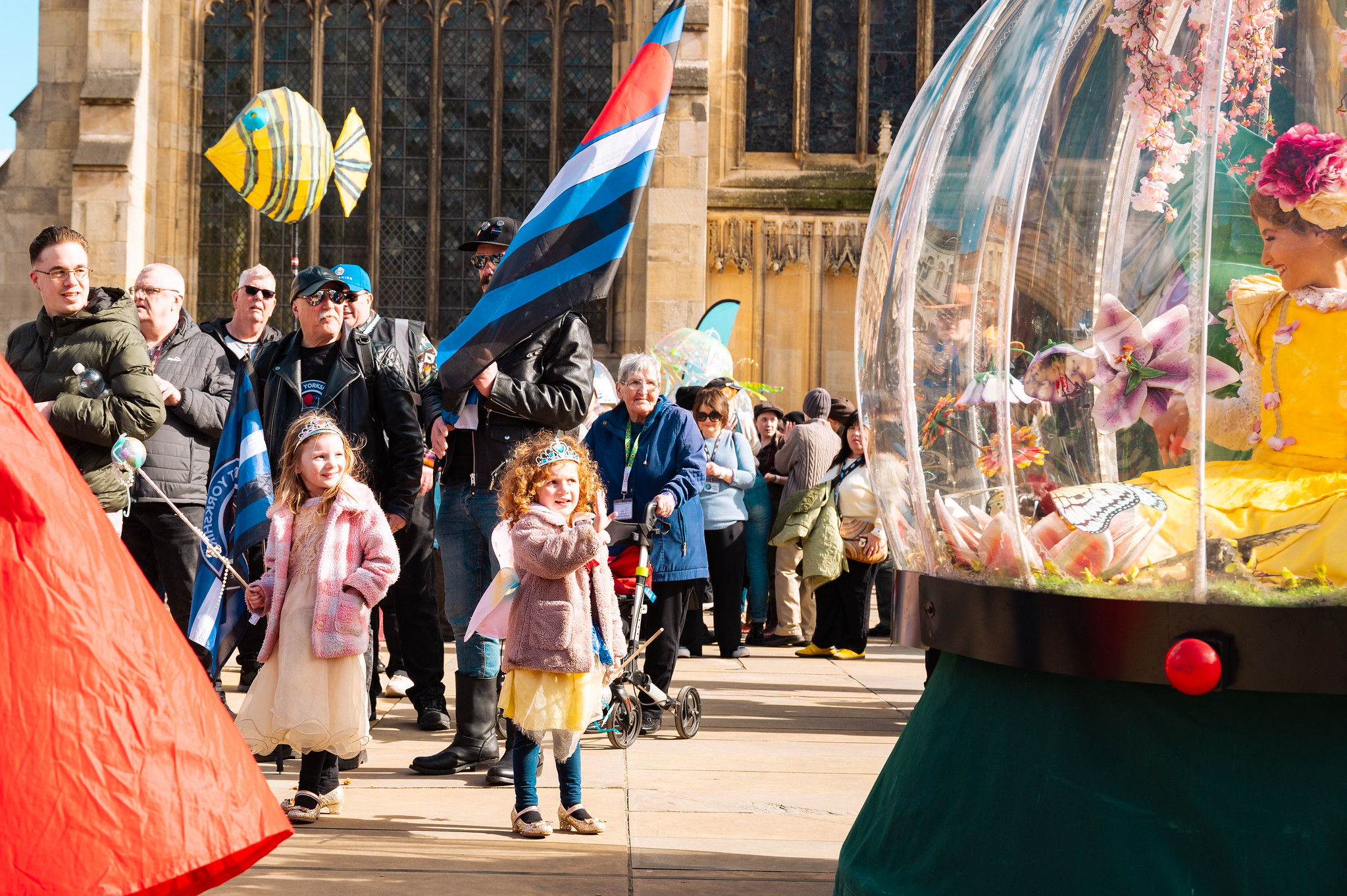 A crowd of people including a young girl waving a flag looking at a character in a snowglobe.